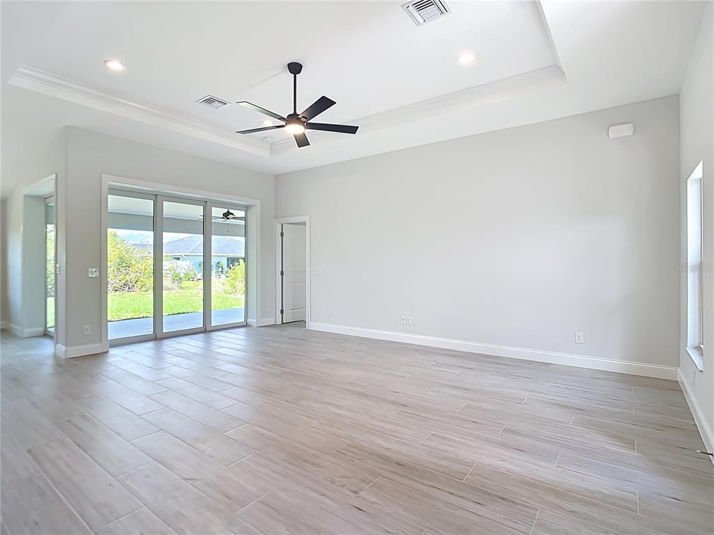 A spacious living room features light tile flooring, a tray ceiling, and sliding glass doors — 13503 AINSWORTH LANE, PORT CHARLOTTE, FL