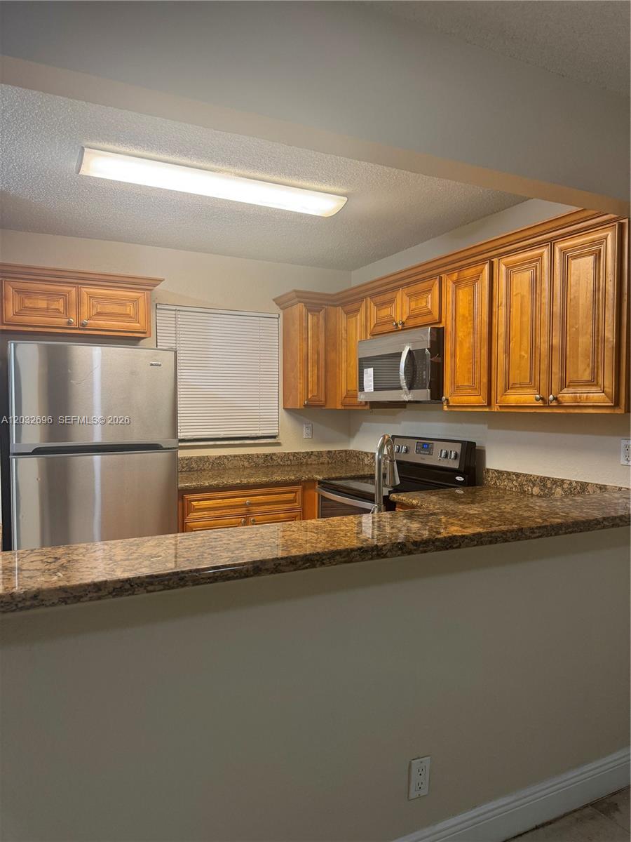 A kitchen features wood cabinets, granite countertops, and stainless steel appliances — 1640 Windorah Way # D, West Palm Beach FL 33411, WEST PALM BEACH, FL