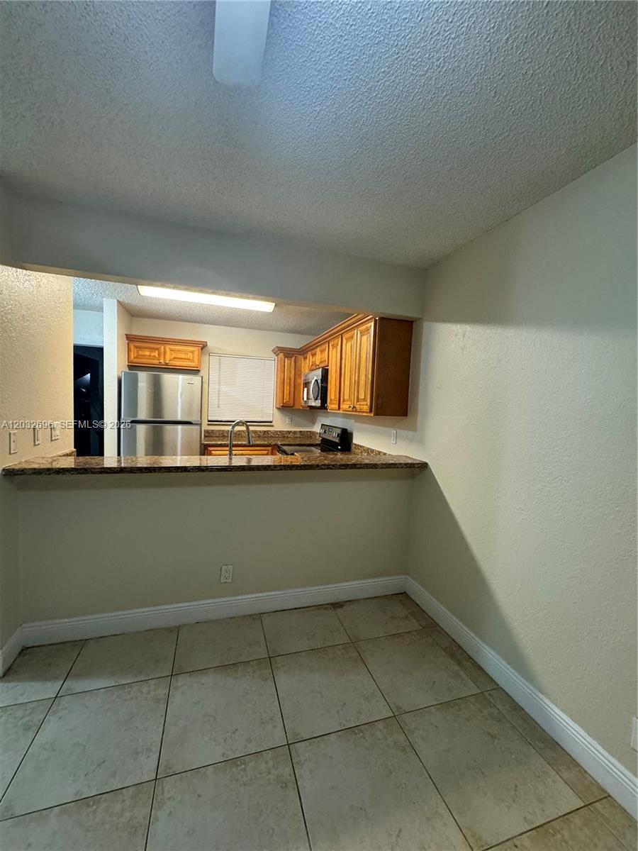 A kitchen with wood cabinets, stainless steel appliances, and a granite breakfast bar — 1640 Windorah Way # D, West Palm Beach FL 33411, WEST PALM BEACH, FL