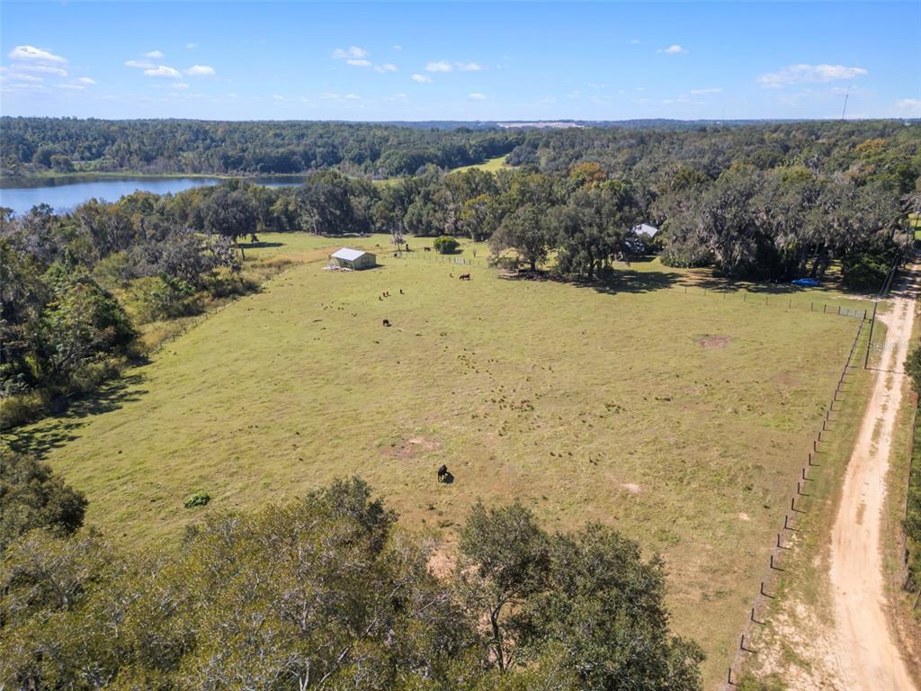 An aerial view shows a large grassy pasture with a small shed and nearby lake — 32854 LISTER ROAD, DADE CITY, FL