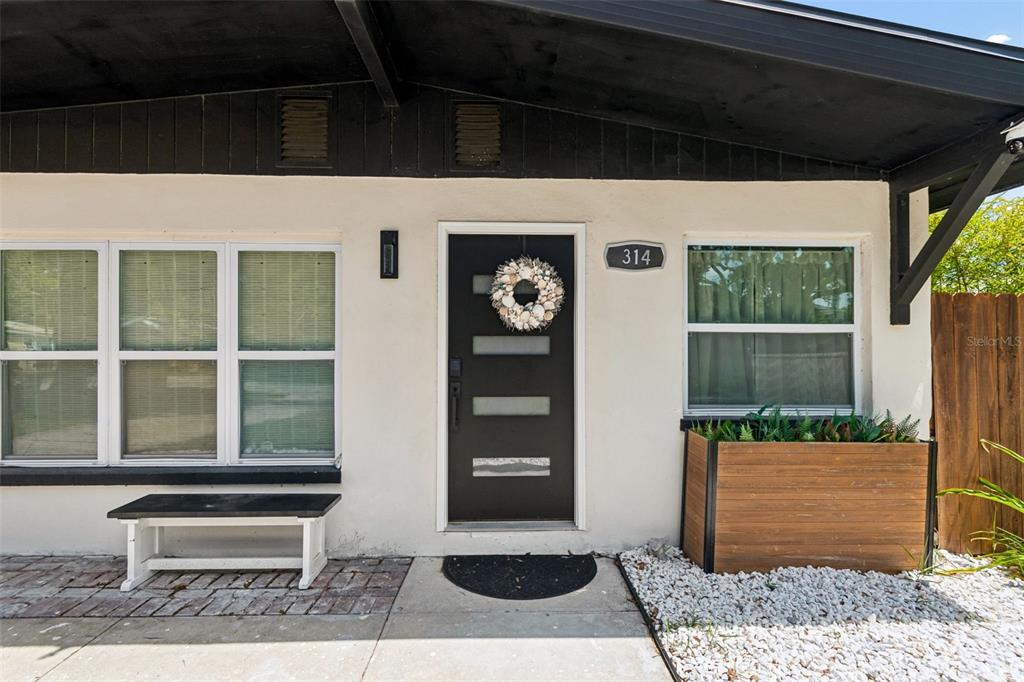 The exterior of a home features a black front door, a bench, and a planter — 314 INDIANA AVENUE, CRYSTAL BEACH, FL