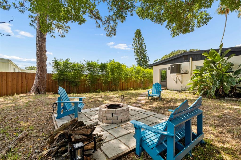 A backyard features a stone fire pit surrounded by blue Adirondack chairs on a patio — 314 INDIANA AVENUE, CRYSTAL BEACH, FL