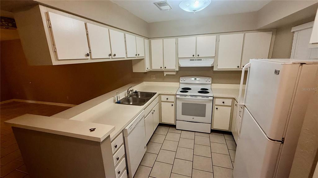 A kitchen features white cabinets, white appliances, a double sink, and light-colored tile flooring — 4411 SW 34TH STREET UNIT 503, GAINESVILLE, FL