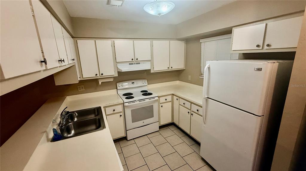 A kitchen features white cabinets, white appliances, a double sink, and light-colored tile flooring — 4411 SW 34TH STREET UNIT 503, GAINESVILLE, FL