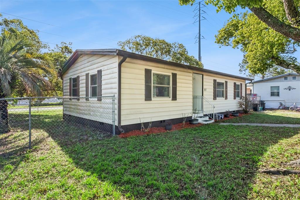 A single-story mobile home with light siding and dark shutters sits on a grassy lot — 217 COLONY DRIVE, CASSELBERRY, FL