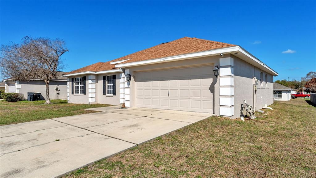 A single-story house with a beige stucco exterior, a two-car garage, and a concrete driveway — 7755 CANTERBURY CIRCLE, LAKELAND, FL