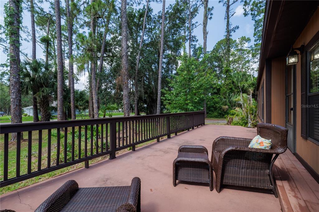 A wooden deck with a railing overlooks a grassy yard surrounded by tall pine trees — 557 NEWTON ROAD, PORT ORANGE, FL