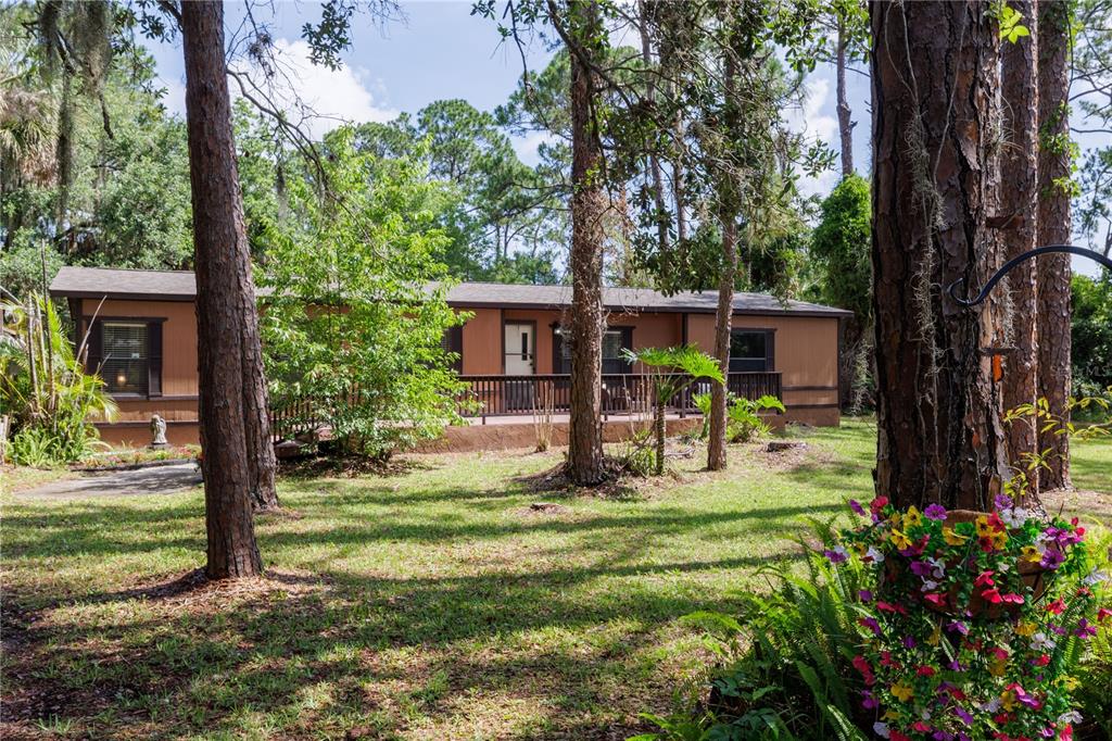 A single-story house with a wooden deck sits among trees in a grassy yard — 557 NEWTON ROAD, PORT ORANGE, FL