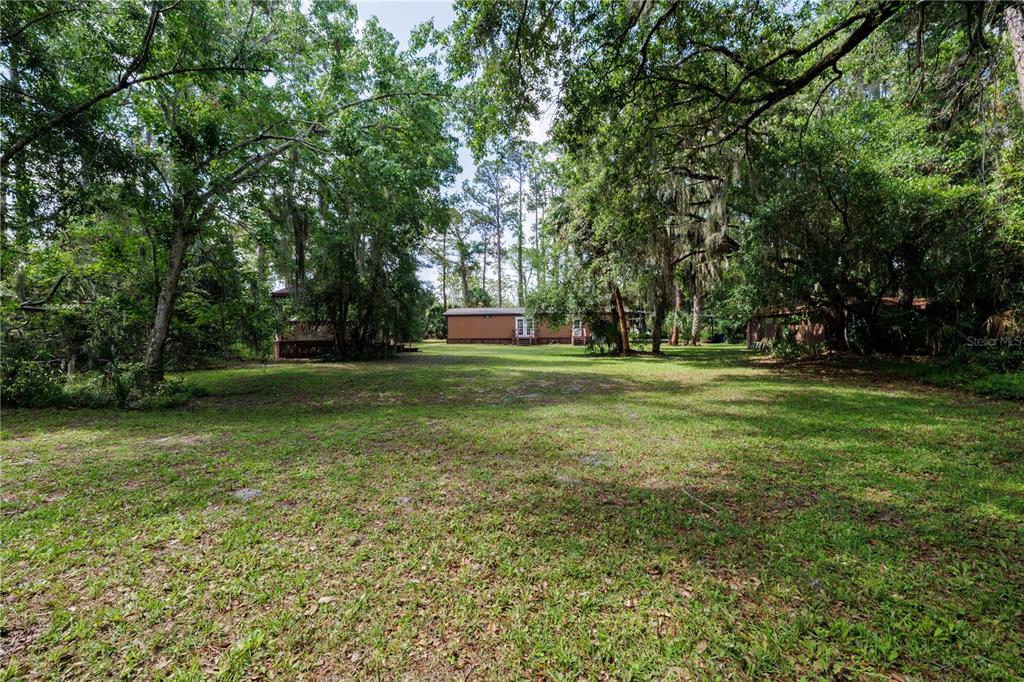 A single-story manufactured home sits at the end of a large, grassy, tree-lined lot — 557 NEWTON ROAD, PORT ORANGE, FL