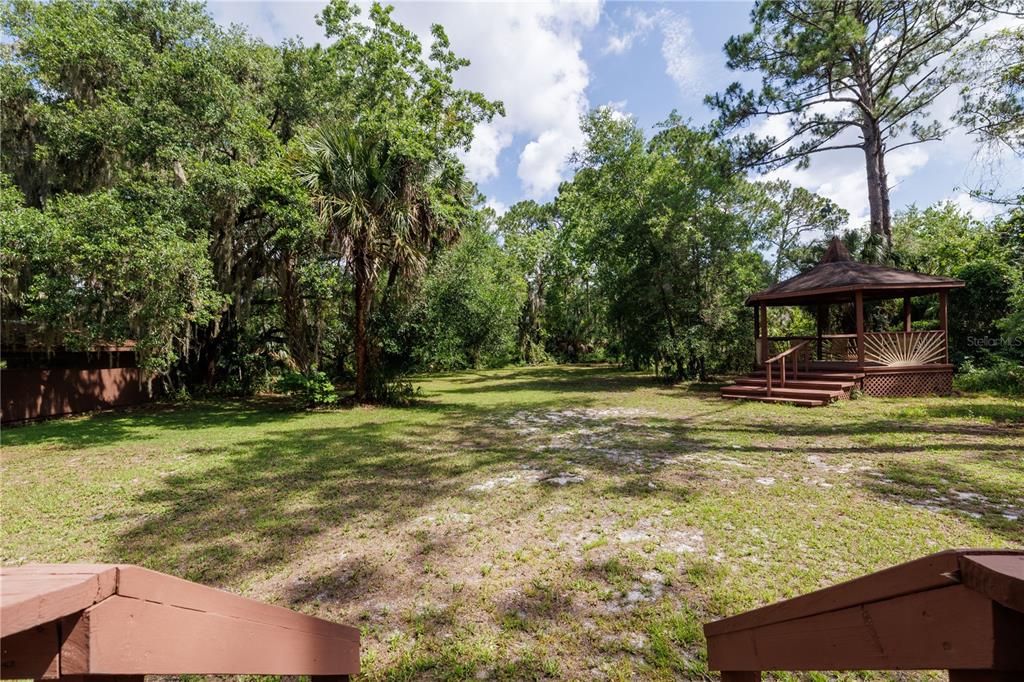 A grassy backyard features a wooden gazebo and mature trees under a cloudy sky — 557 NEWTON ROAD, PORT ORANGE, FL