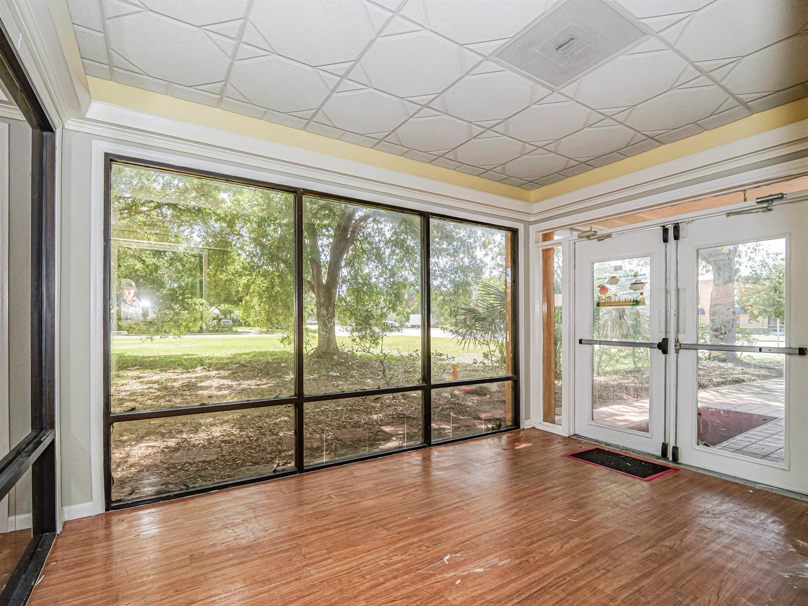 A sunroom with wood-look flooring, a patterned drop ceiling, and large windows overlooking trees — 3660 20th Street, Vero Beach FL 32960, VERO BEACH, FL