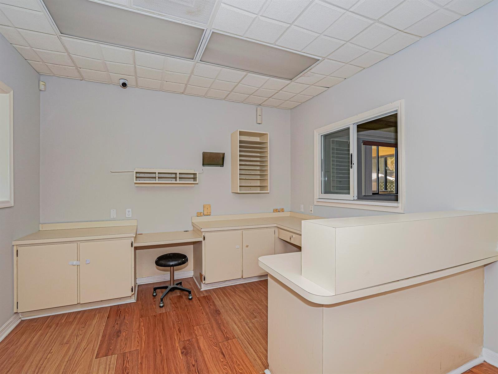 An office reception area features light-colored cabinetry, a desk, a rolling stool, and wood flooring — 3660 20th Street, Vero Beach FL 32960, VERO BEACH, FL