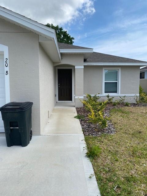 A beige house exterior features a dark front door, a concrete walkway, and a trash bin — 20 BUTTONWOOD LANE, PALM COAST, FL