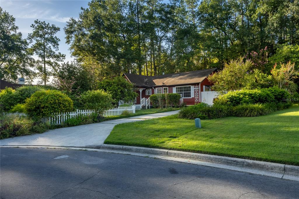 A red house with a white picket fence sits behind a driveway and green lawn — 10709 NW 31ST PLACE, GAINESVILLE, FL