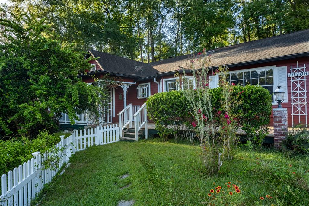 A red house with a white picket fence, front porch, and steps leading to the entrance — 10709 NW 31ST PLACE, GAINESVILLE, FL