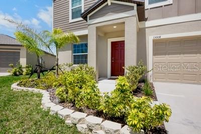 A two-story house exterior features a red front door, a garage, and a landscaped garden — 13008 MERLOT SUNSTONE COVE, PARRISH, FL