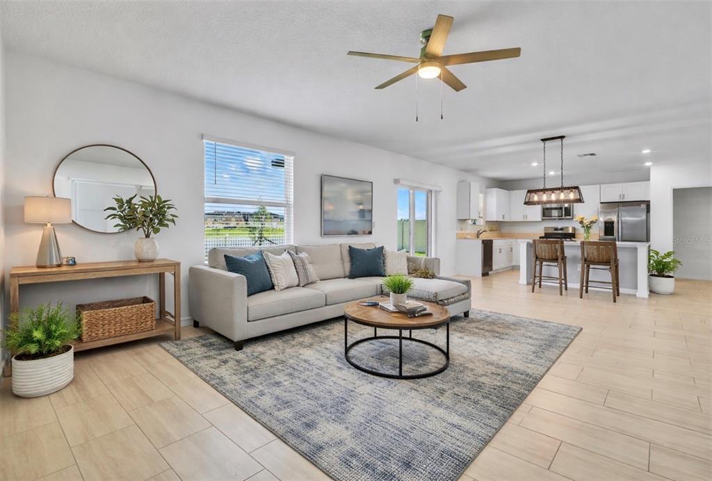 An open-concept living room and kitchen featuring light tile flooring and a neutral color palette — 13008 MERLOT SUNSTONE COVE, PARRISH, FL