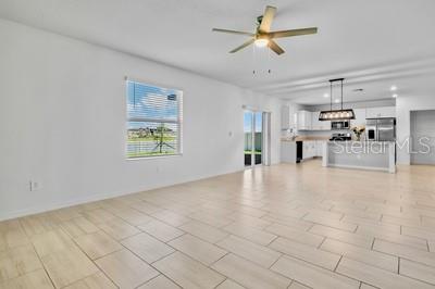 An open-concept living area features light-colored tile flooring, a ceiling fan, and a kitchen — 13008 MERLOT SUNSTONE COVE, PARRISH, FL