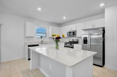 A modern kitchen features white cabinets, a large quartz island, and stainless steel appliances — 13008 MERLOT SUNSTONE COVE, PARRISH, FL