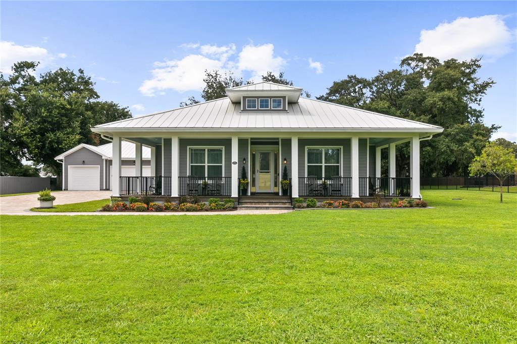A single-story house with a metal roof, wrap-around porch, and detached garage on a lawn — 4421 JIM BRANCH ROAD, KISSIMMEE, FL