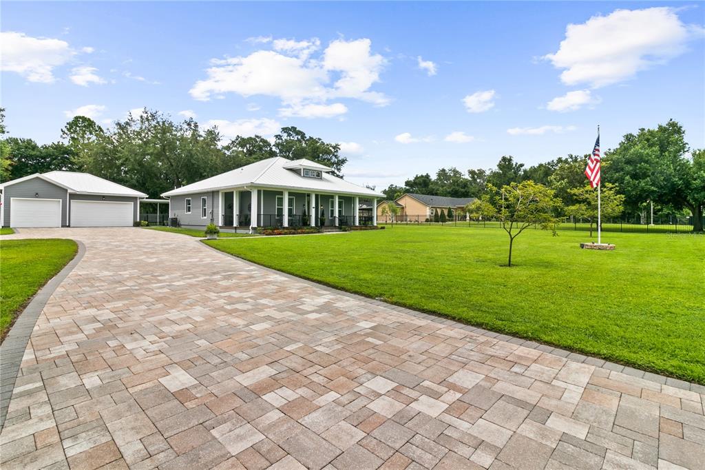 A gray house with a metal roof and a large paver driveway under a blue sky — 4421 JIM BRANCH ROAD, KISSIMMEE, FL