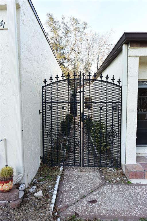 A black metal gate stands between two white stucco walls leading to a walkway — 5645 HAMILTON HARBOR DRIVE, NEW PORT RICHEY, FL