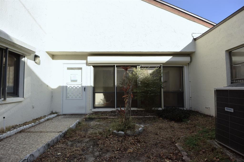 A white exterior wall features a front door and a large window with a shutter — 5645 HAMILTON HARBOR DRIVE, NEW PORT RICHEY, FL
