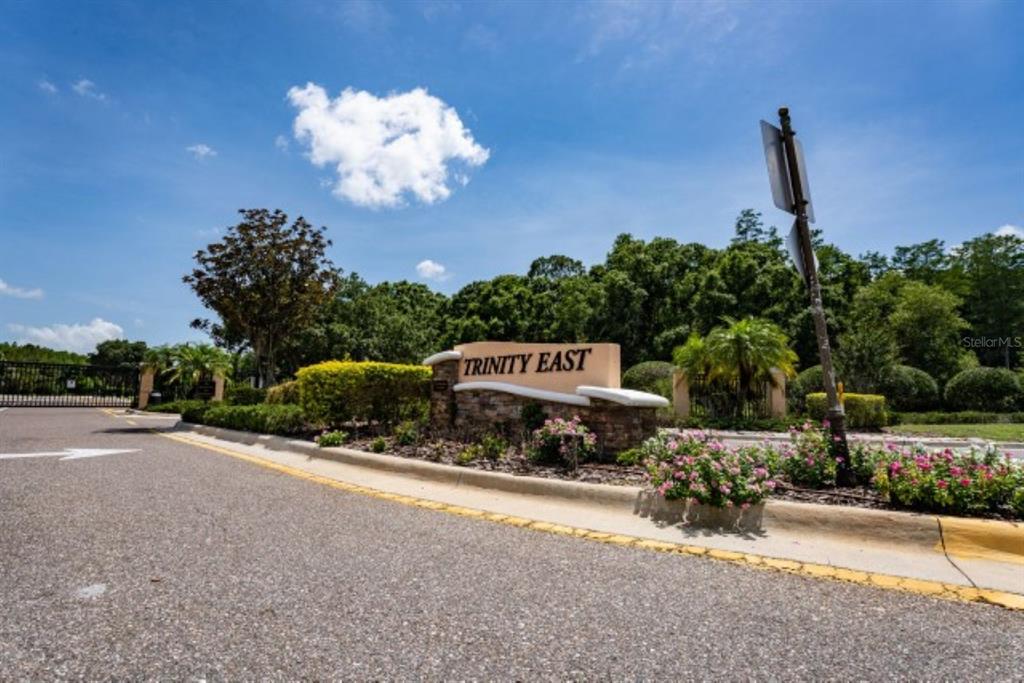 A stone monument sign for Trinity East stands at the entrance to a gated community — 1038 KETZAL DRIVE, TRINITY, FL