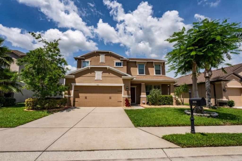 A two-story suburban house with a tan stucco exterior, a two-car garage, and a driveway — 1038 KETZAL DRIVE, TRINITY, FL
