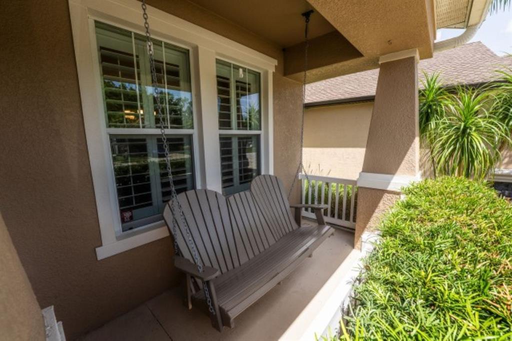 A covered front porch features a hanging wooden bench swing and white-trimmed windows — 1038 KETZAL DRIVE, TRINITY, FL