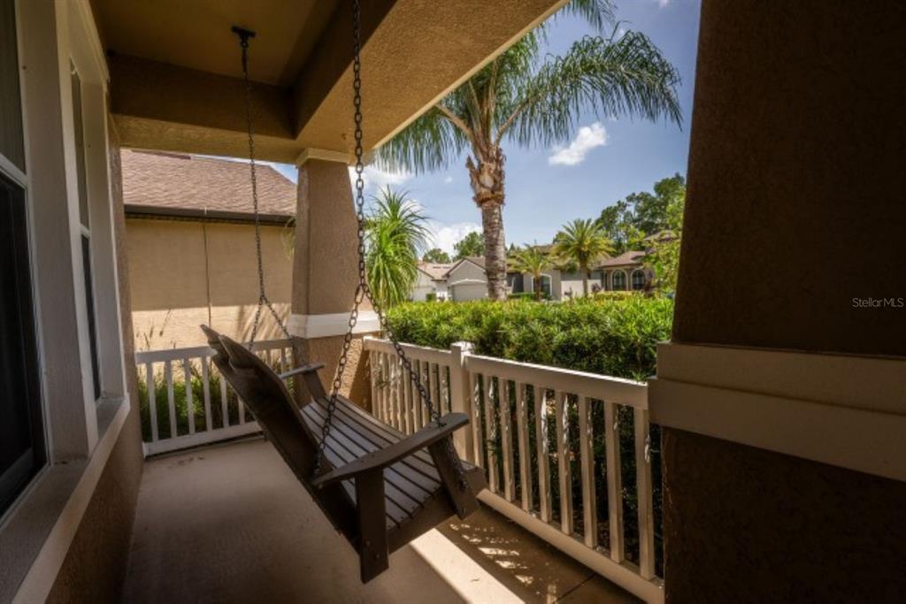 A covered porch features a wooden swing hanging from the ceiling and a white railing — 1038 KETZAL DRIVE, TRINITY, FL