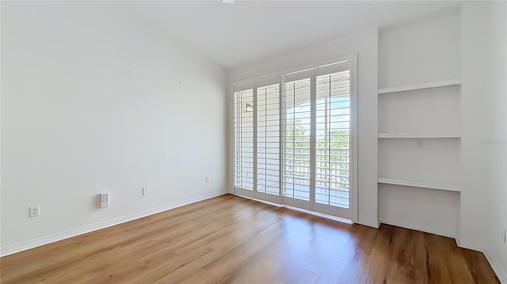 An empty room features light wood flooring, white walls, built-in shelving, and sliding glass doors — 2615 MAITLAND CROSSING WAY UNIT 303, ORLANDO, FL