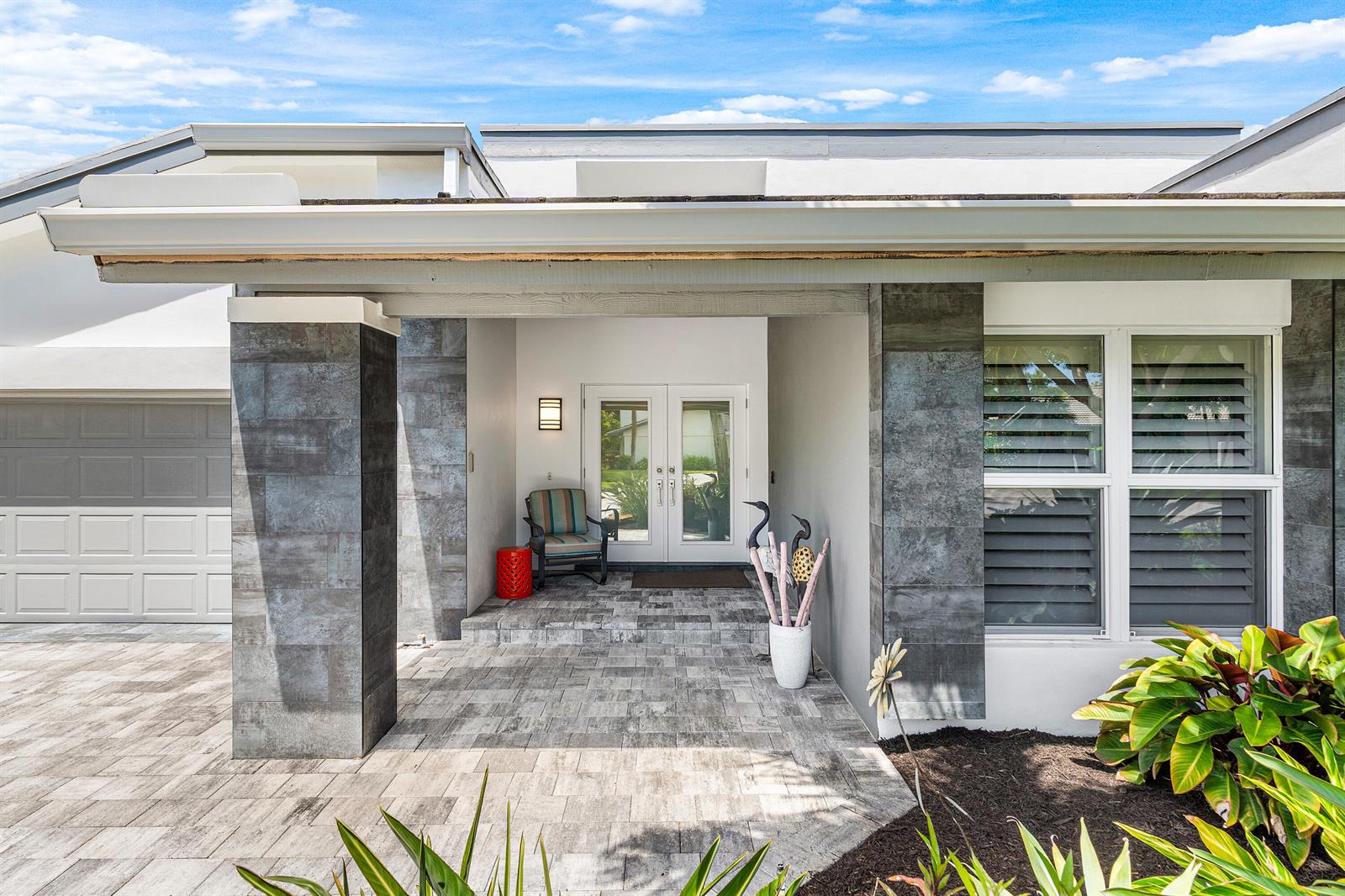 The exterior of a house features a stone-tiled entryway, double glass doors, and a paved driveway — 632 Lakewoode Circle W, Delray Beach FL 33445, DELRAY BEACH, FL