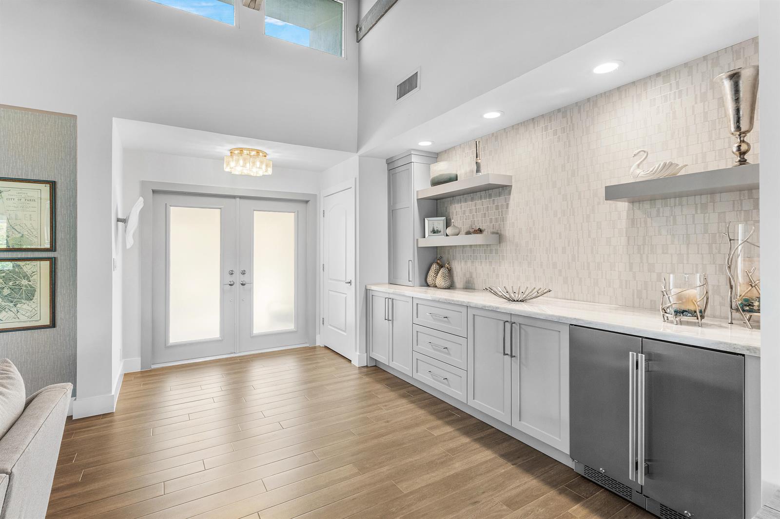 A bright entryway features light wood flooring, a wet bar with gray cabinetry, and double doors — 632 Lakewoode Circle W, Delray Beach FL 33445, DELRAY BEACH, FL