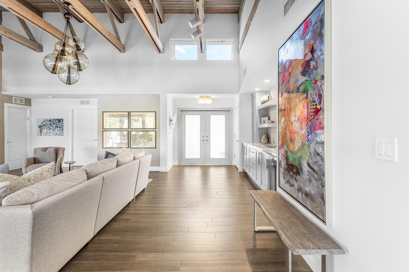 A spacious living room features vaulted wood-beam ceilings, light wood flooring, and a large abstract painting — 632 Lakewoode Circle W, Delray Beach FL 33445, DELRAY BEACH, FL
