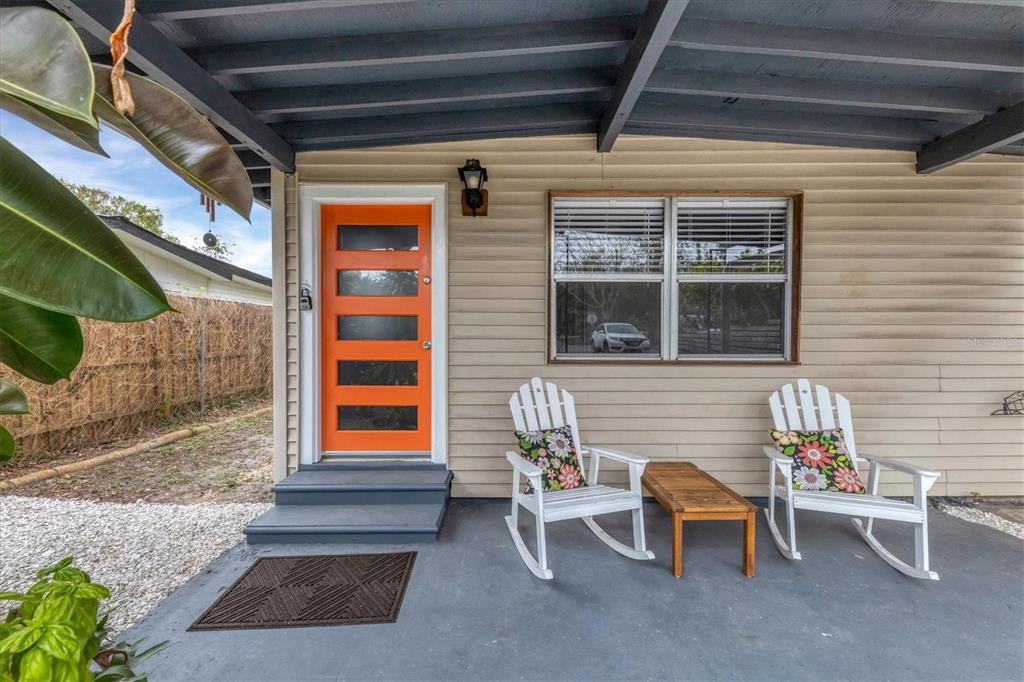 A covered porch features a bright orange front door, two white rocking chairs, and siding — 2305 NOVUS STREET, SARASOTA, FL
