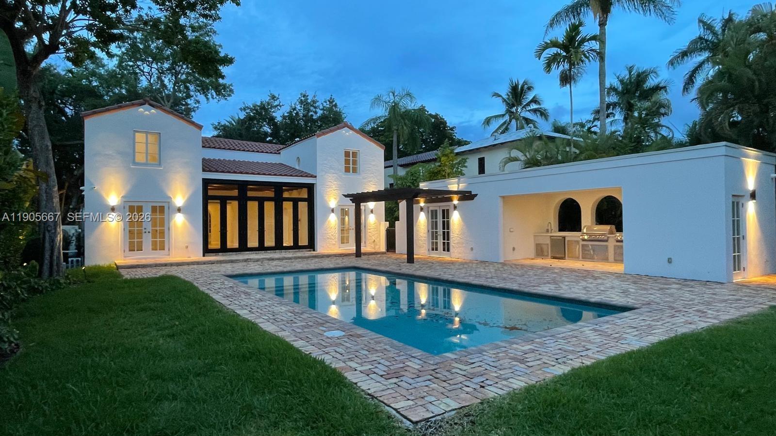 A white stucco house with a swimming pool and an outdoor kitchen at dusk — 4100 Monserrate St, Coral Gables FL 33146, CORAL GABLES, FL