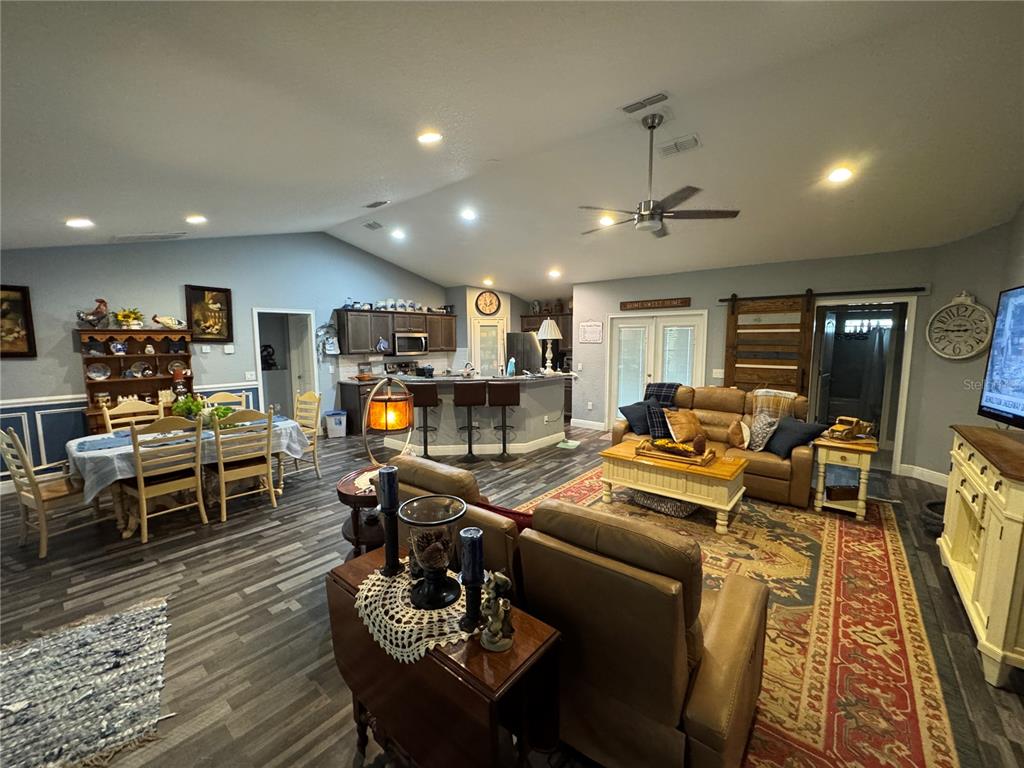 An open-concept living and dining area features wood-look flooring, a kitchen island, and vaulted ceilings — 16361 SE 80TH TERRACE, SUMMERFIELD, FL