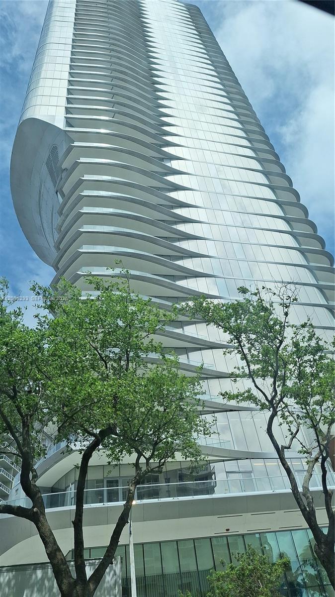 A low-angle view of a modern, curved glass skyscraper with prominent horizontal balcony tiers — 175 se 25 rd # 2803, Miami FL 33129, MIAMI, FL