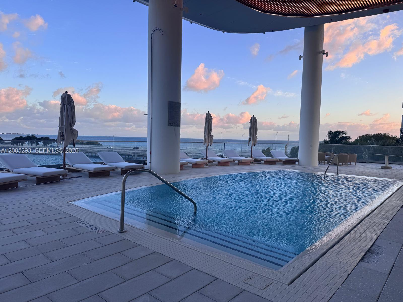 A swimming pool with lounge chairs sits on a terrace overlooking the ocean at sunset — 175 se 25 rd # 2803, Miami FL 33129, MIAMI, FL