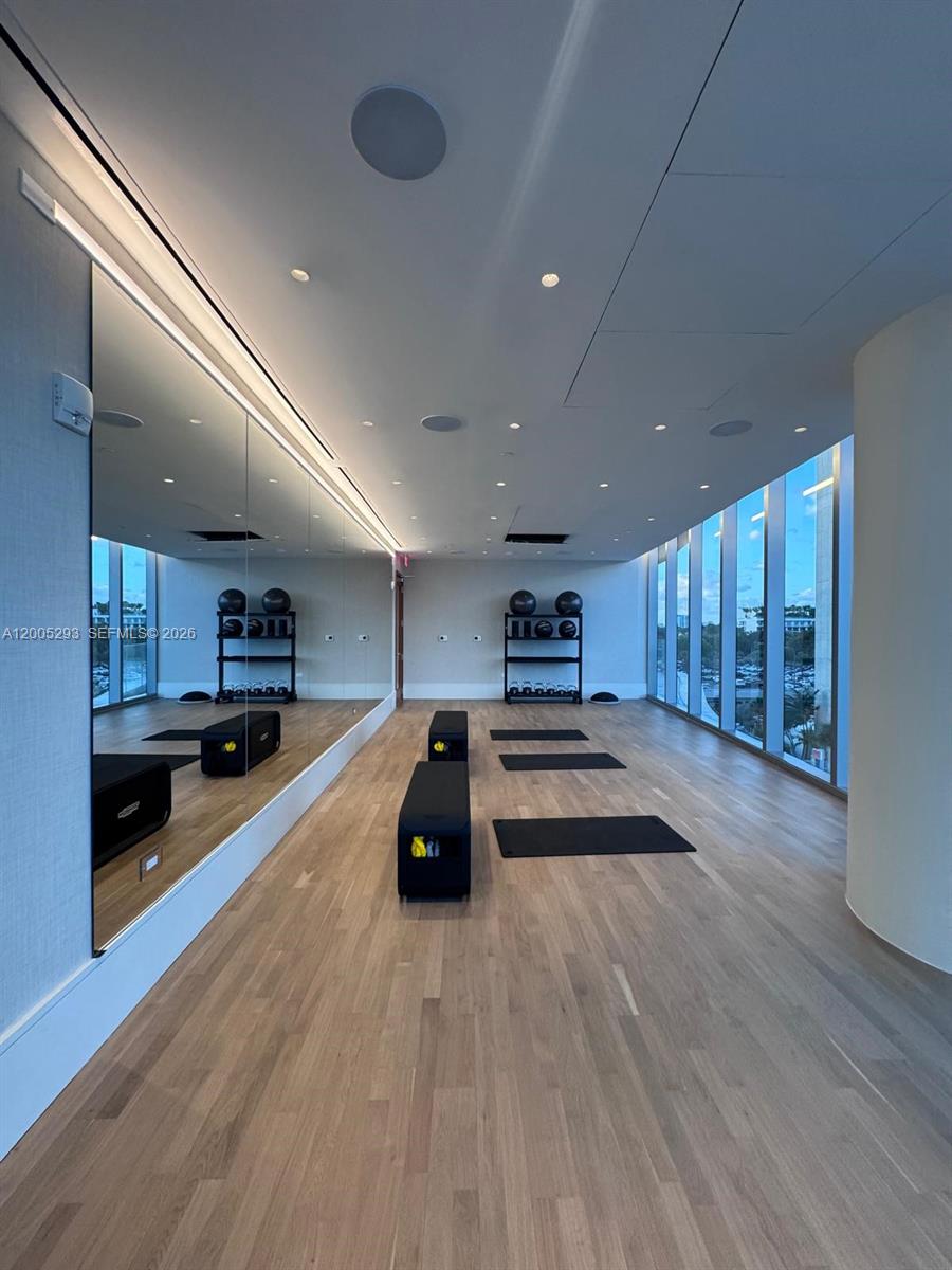 A modern fitness studio features wood flooring, floor-to-ceiling windows, a large wall mirror, and exercise equipment — 175 se 25 rd # 2803, Miami FL 33129, MIAMI, FL