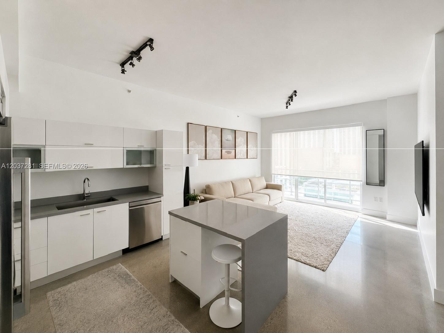 A modern studio apartment features a kitchen with white cabinetry, a gray island, and living area — 133 NE 2nd Ave # 1508, Miami FL 33132, MIAMI, FL