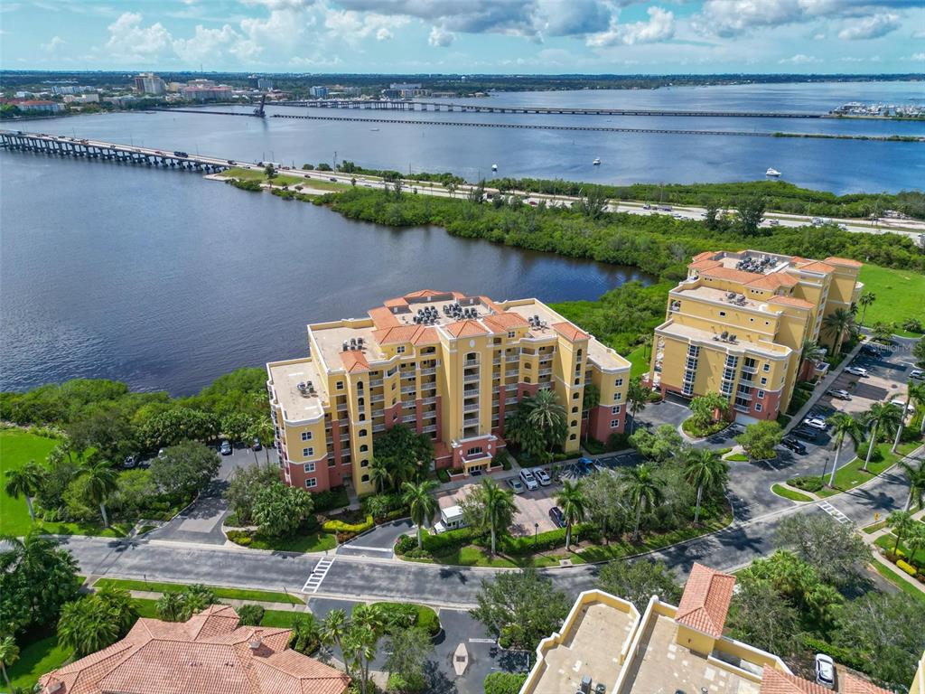 An aerial view shows two multi-story apartment buildings near a large body of water — 615 RIVIERA DUNES WAY UNIT 107, PALMETTO, FL