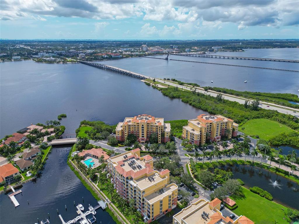 An aerial view shows waterfront apartment buildings, a bridge, and a marina in Florida — 615 RIVIERA DUNES WAY UNIT 107, PALMETTO, FL