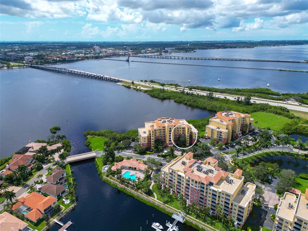 An aerial view shows waterfront apartment buildings, a bridge, and a pool in a coastal area — 615 RIVIERA DUNES WAY UNIT 107, PALMETTO, FL