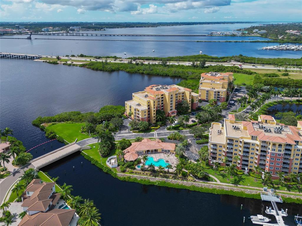 An aerial view shows waterfront condominium buildings, a swimming pool, and a bridge over water — 615 RIVIERA DUNES WAY UNIT 107, PALMETTO, FL