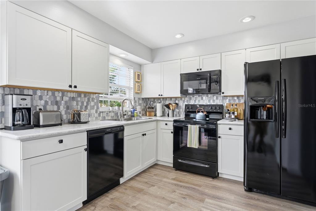 A kitchen with white cabinets, black appliances, a patterned backsplash, and light wood-look flooring — 3625 57TH AVENUE DRIVE W UNIT 43, BRADENTON, FL