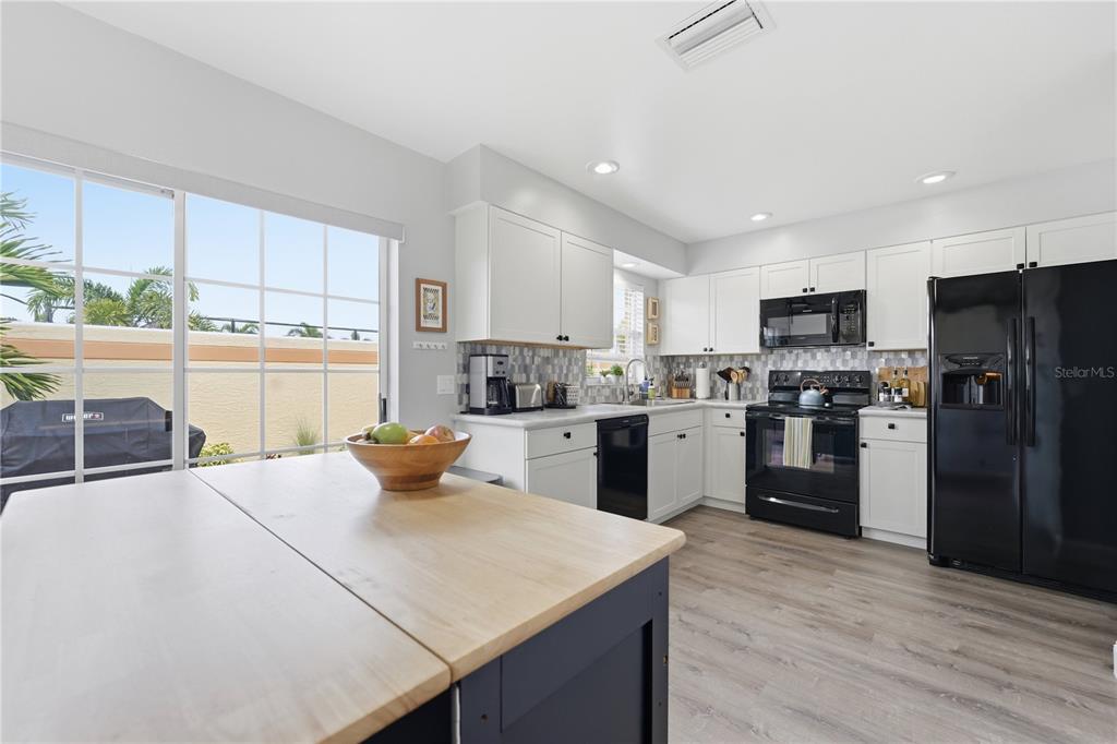 A kitchen features white cabinets, black appliances, a wooden island, and a sliding glass door — 3625 57TH AVENUE DRIVE W UNIT 43, BRADENTON, FL