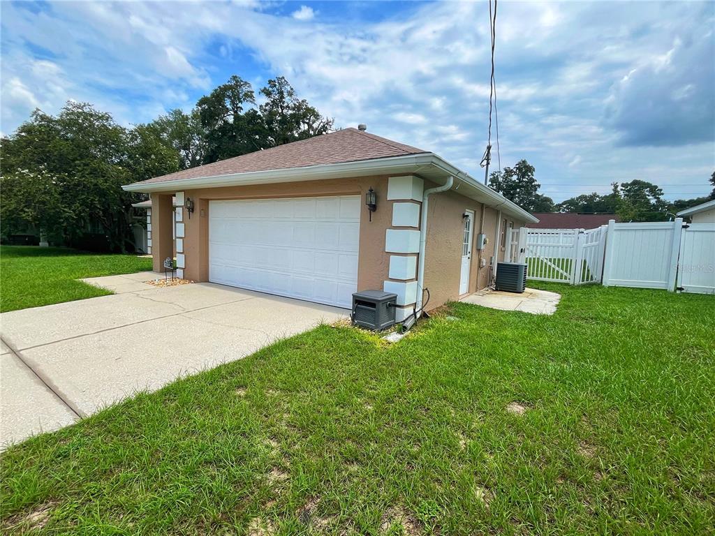 A detached garage with a white door, tan stucco walls, and a white vinyl fence — 3201 NE 42ND PLACE, OCALA, FL