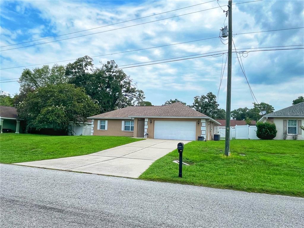 A single-story house with a tan exterior, a white garage door, and a concrete driveway — 3201 NE 42ND PLACE, OCALA, FL